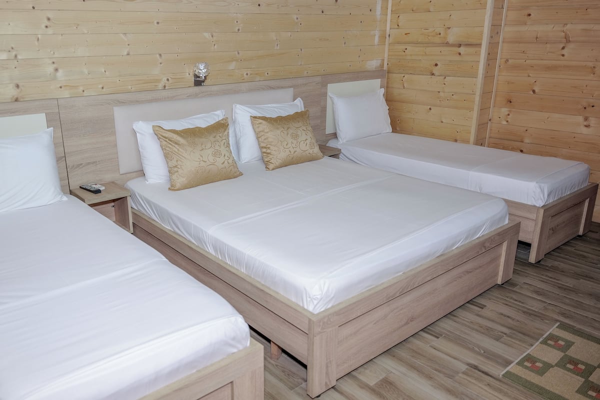 A room with two single beds and a larger bed, all with white linens.