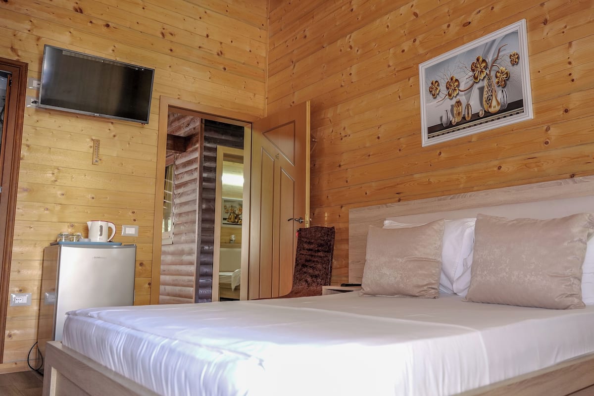 A wooden-paneled room with a bed, a TV, and a painting of flowers.