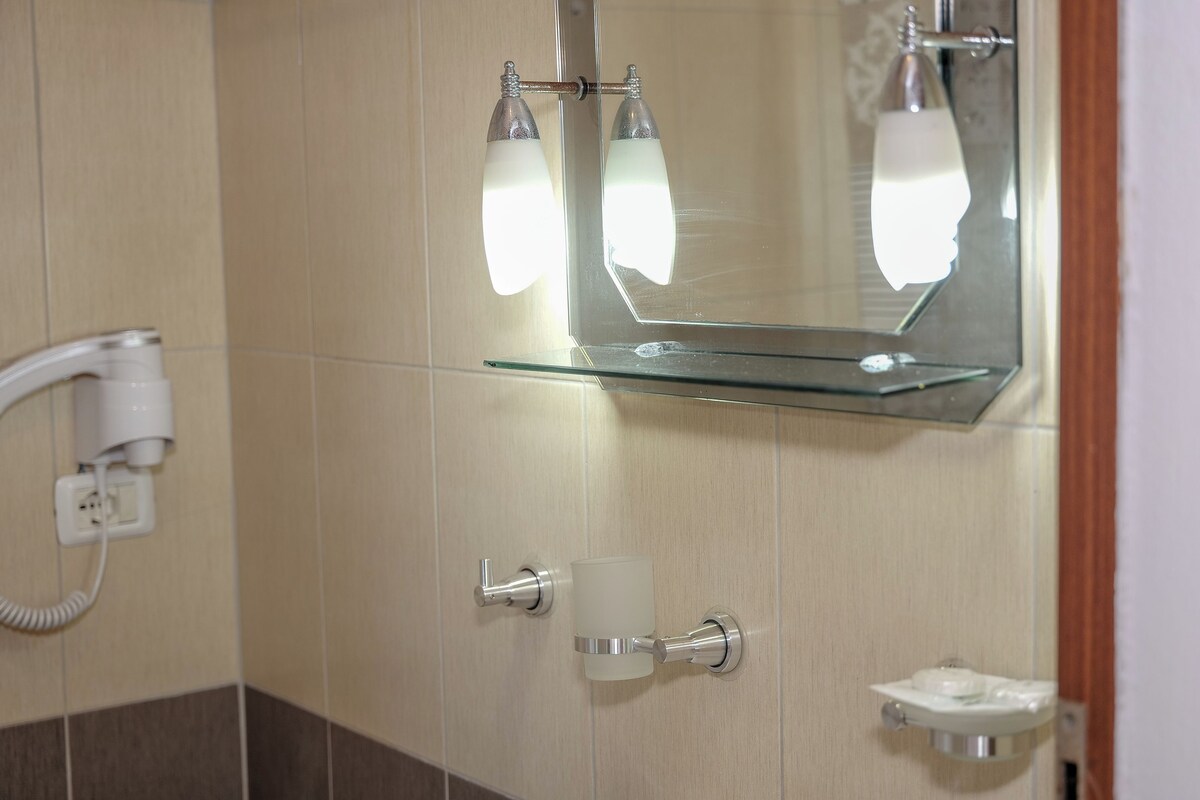 A bathroom with a glass shelf, a hairdryer, a towel rack, and a soap dispenser.