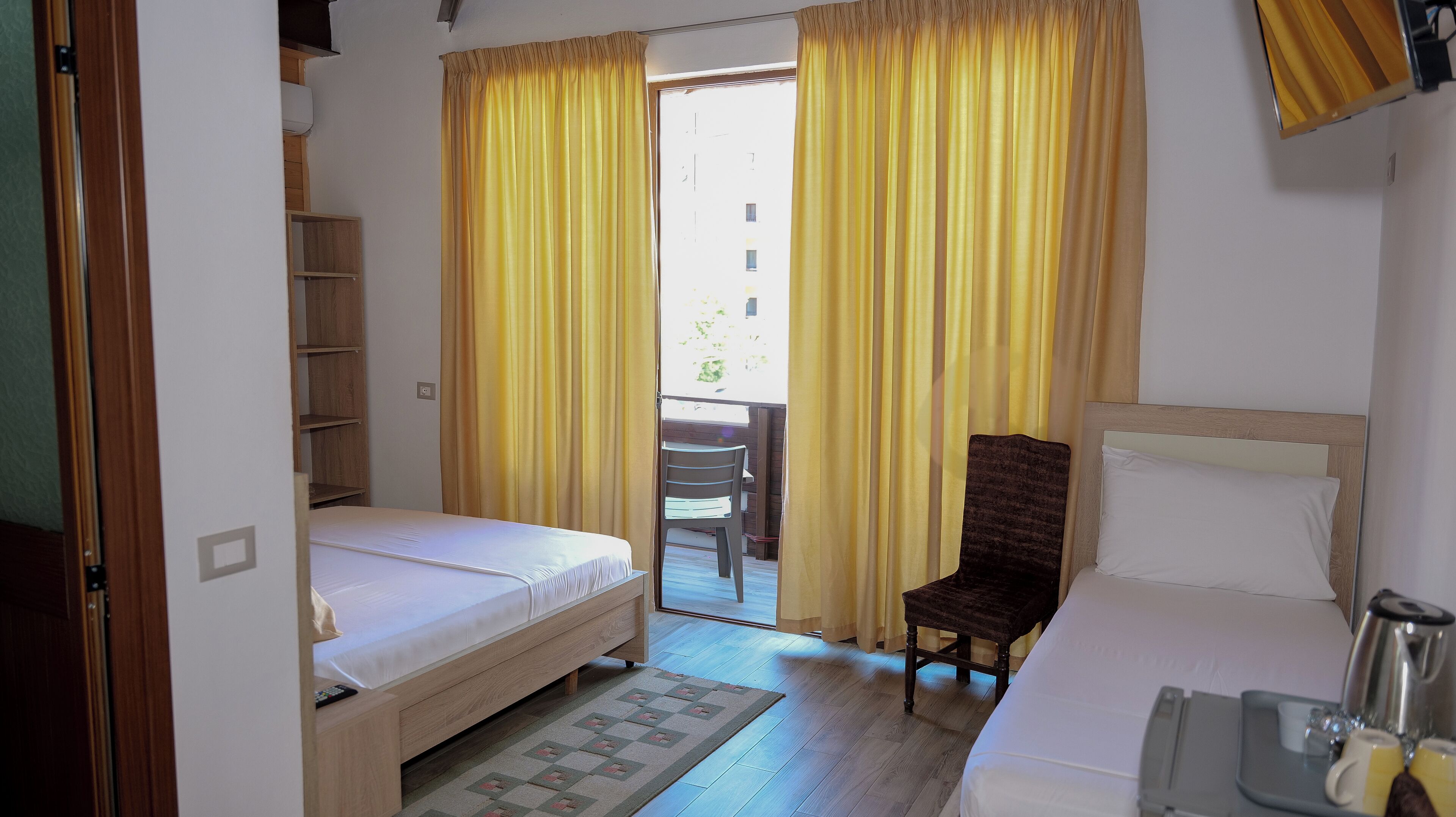 Une chambre d’hôtel avec un lit, une chaise, un bureau et une vue par la fenêtre, qui est ornée de rideaux jaunes.