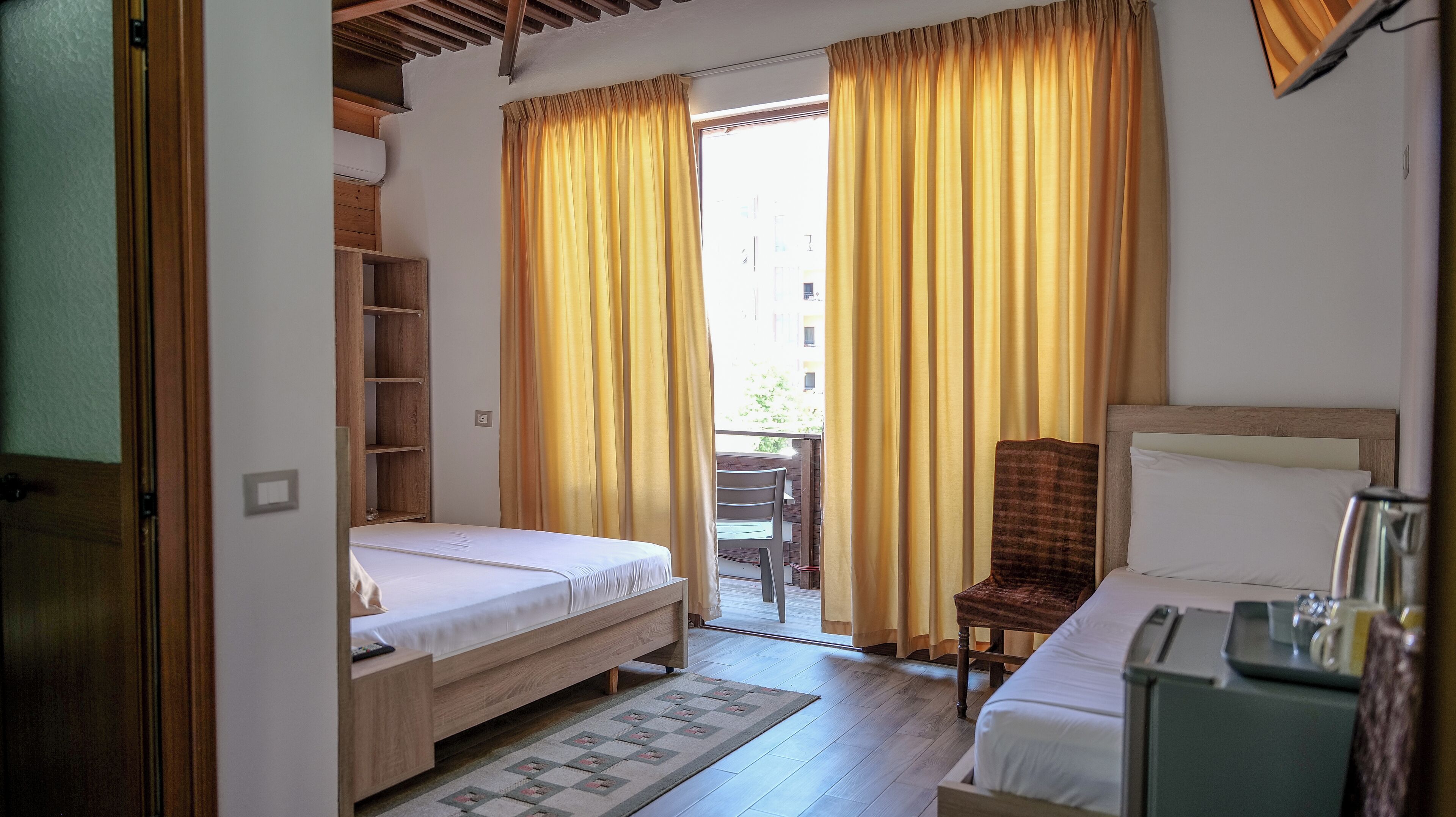 Een slaapkamer met twee bedden, een houten garderobe, een stoel en een klein tafeltje.