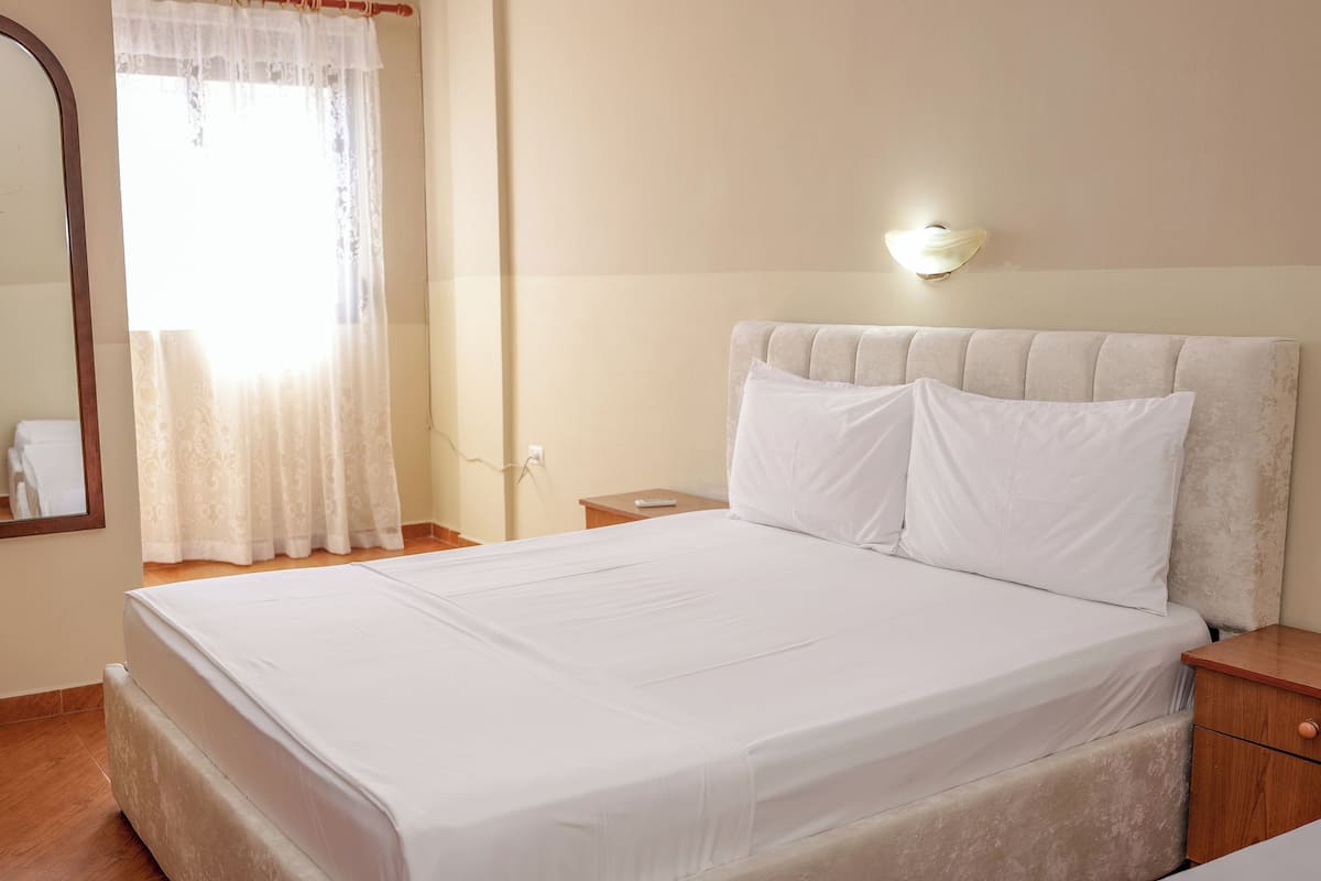 A neatly made bed with white linens, a bedside table with a lamp, and a large mirror on the wall.
