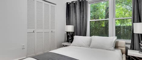 A neatly arranged bedroom with a bed, bedside table, lamp, and window with curtains.