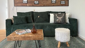 A green sofa with a wooden coffee table and a white pouf in front. - ALLGÄUHERZ - Great apartment in Nesselwang - KÖNIGSKARTE (Nesselwang)