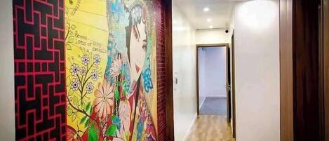 A hallway with a colorful mural on the left wall, a wooden floor, and a door at the end.