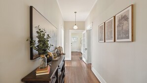 Ein Flur mit Holzboden, einer hängenden Pendelleuchte, gerahmten Bildern an der Wand und einer Pflanze auf einem Tisch.