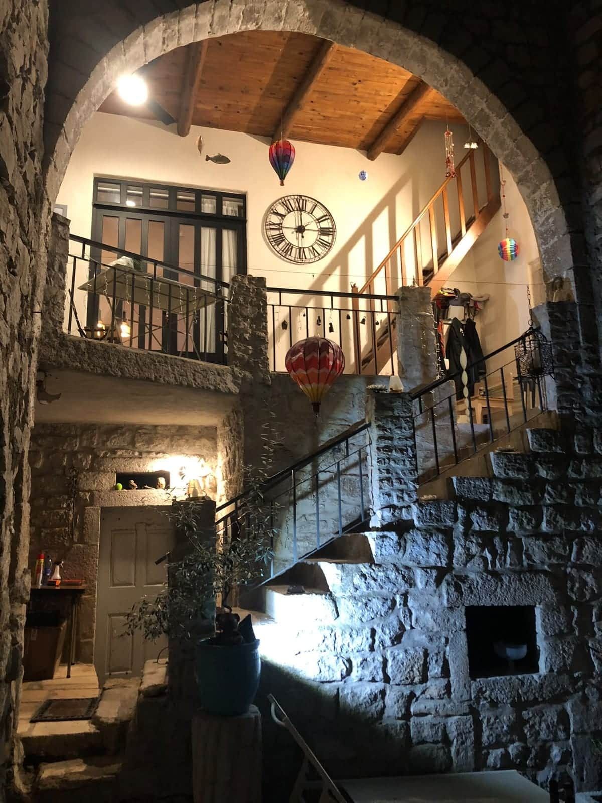 Un escalier en pierre avec un plafond en bois, une horloge et un balcon doté d’une balustrade.