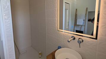 Un baño moderno con un lavamanos blanco, tocador de madera y un espejo grande.
