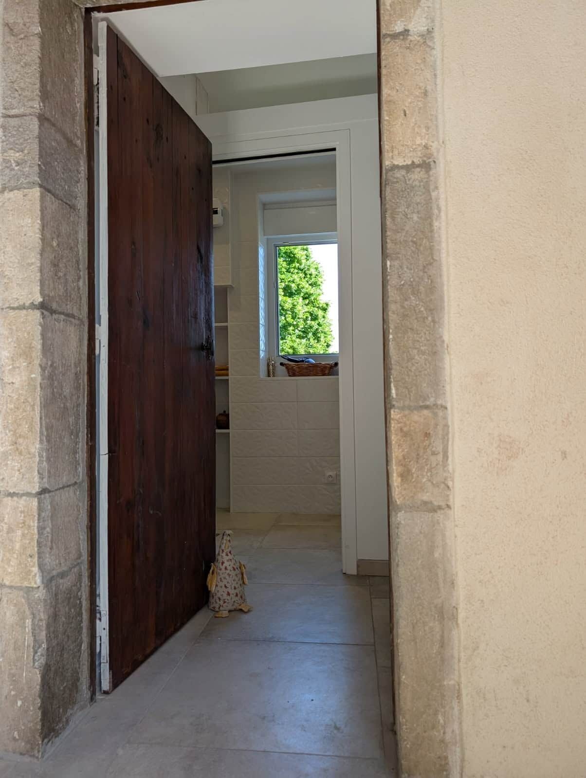 Un couloir étroit, avec une porte en bois sur la gauche et une fenêtre au fond.