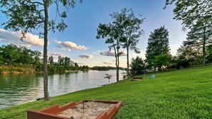 A wooden raised garden bed with sand, a grassy area, and a lake with trees in the background.