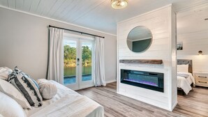 A bedroom with a bed, a fireplace, a large mirror, and a view of a lake through the window.
