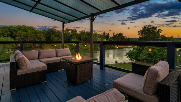 An outdoor deck with a fire feature, seating, and a view of a lake at sunset.