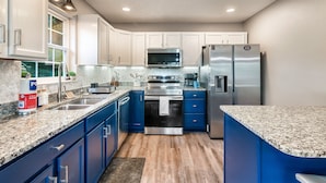A modern kitchen with blue cabinets, granite countertops, stainless steel appliances, and a window providing natural light.