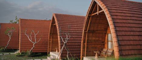 A row of wooden cabins with pitched roofs, each featuring a small porch and a table and chair set.