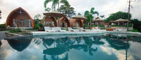 A poolside area with wooden cabanas and lounge chairs.