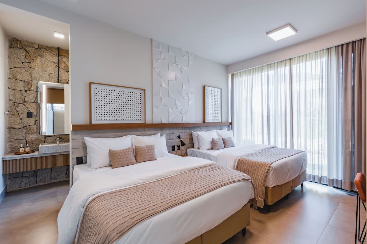 Habitación de hotel con dos camas, un detalle de pared de piedra, un ventanal con cortinas y una decoración moderna.
