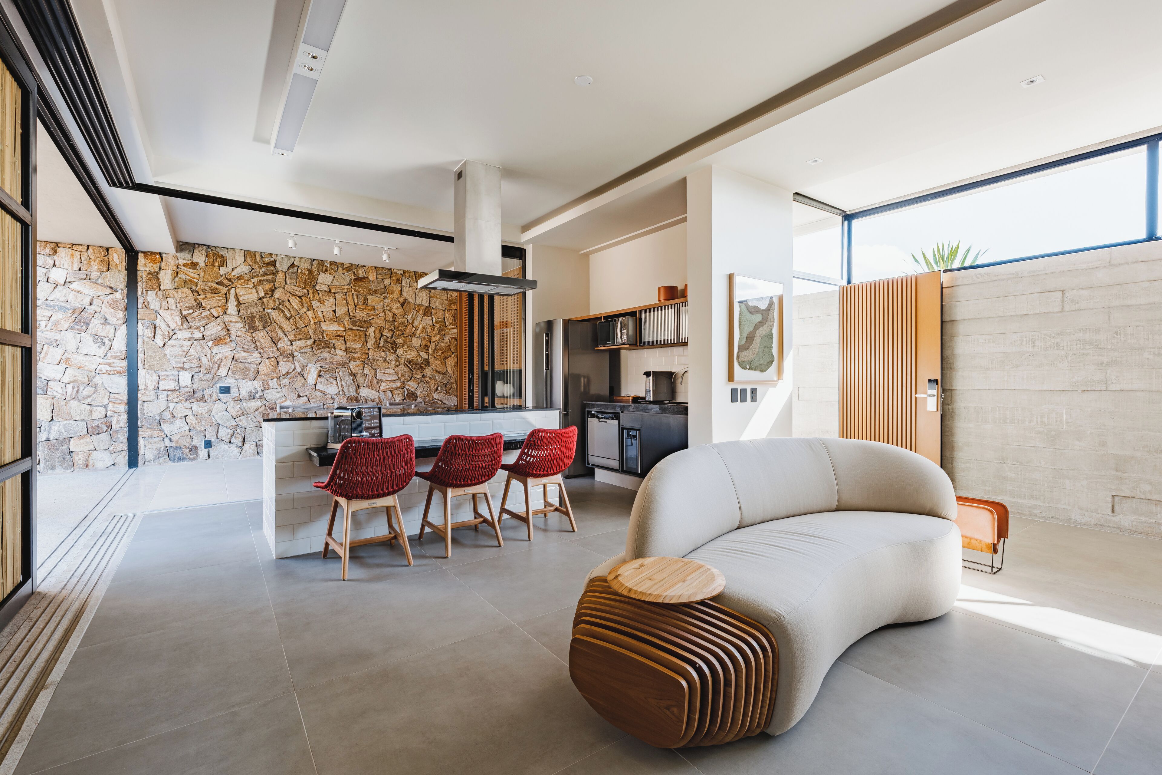 A spacious living area with a stone wall, a modern kitchen, and a dining area with red chairs.