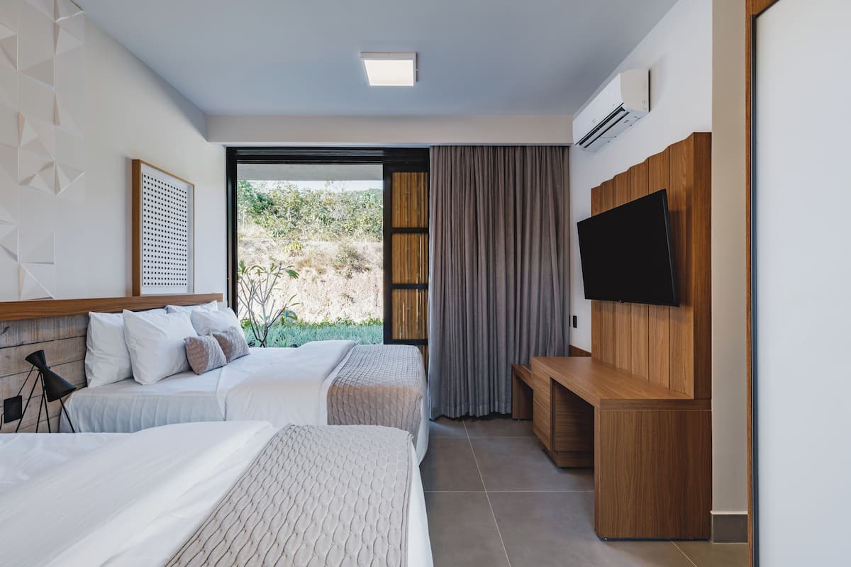 Habitación de hotel moderna con dos camas, un televisor de pantalla plana, un escritorio de madera y un ventanal con vistas a zonas verdes.