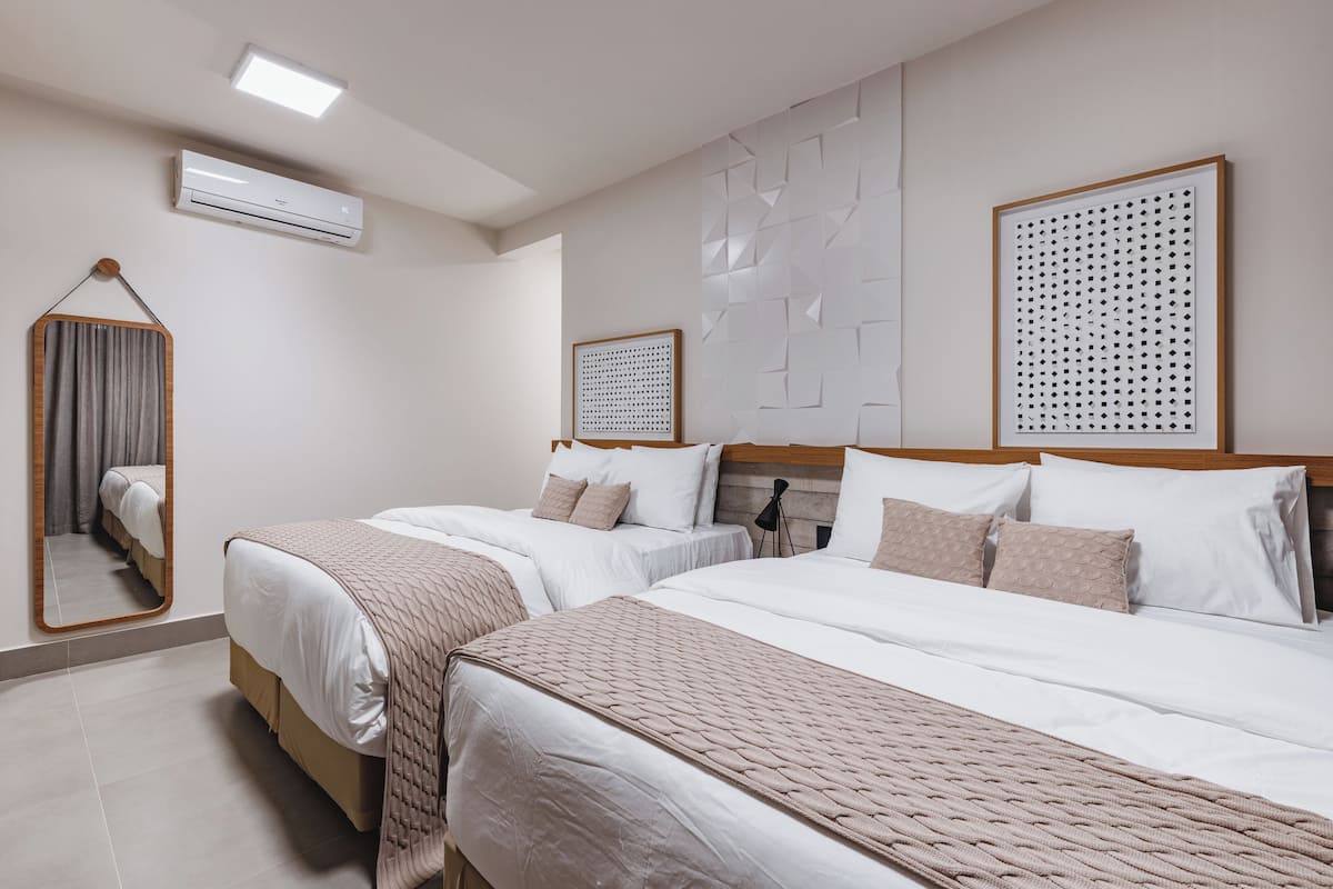 Una habitación de hotel con dos camas, un espejo, aire acondicionado y un panel de pared geométrico.
