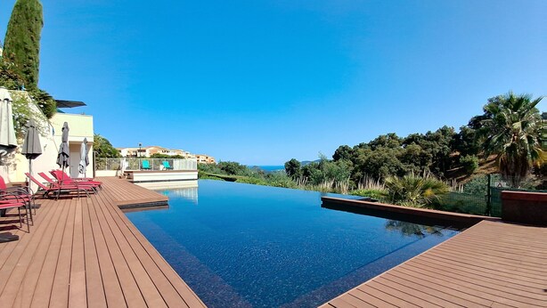 Cielo azul despejado, una terraza de madera y una piscina con vistas al océano y las colinas.