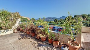 Una terraza en la azotea con plantas en macetas y vistas a coches estacionados y colinas al lejano.