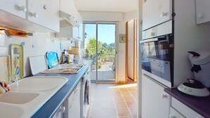 Una cocina estrecha con lavadora, un horno grande y vistas al jardín a través de un ventanal.