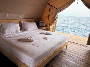 A bed with white linens, a bedside table with a lamp, and a view of the sea.
