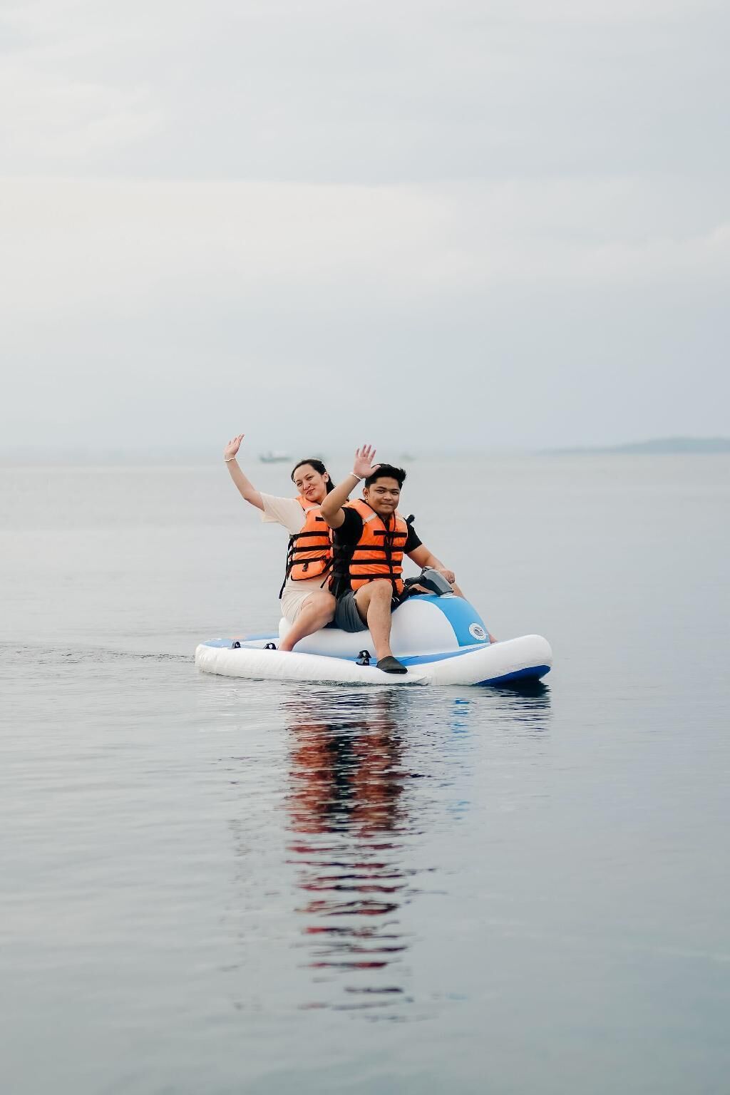 Zwei Personen auf einem Wasserfahrzeug mit Rettungswesten, die auf ruhigem Wasser treiben.
