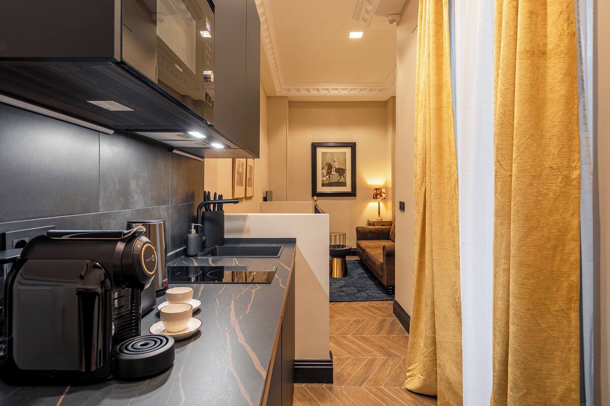 Una cocina moderna con cafetera, pileta y encimera. Se observa un cuadro en la pared y una lámpara sobre una mesita auxiliar.