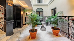 A spacious indoor area with a tiled floor, two large potted plants, a small fountain, and a decorative wall with patterned tiles. - Casa 1862 Heritage Suites by Stay Unique (Seville)