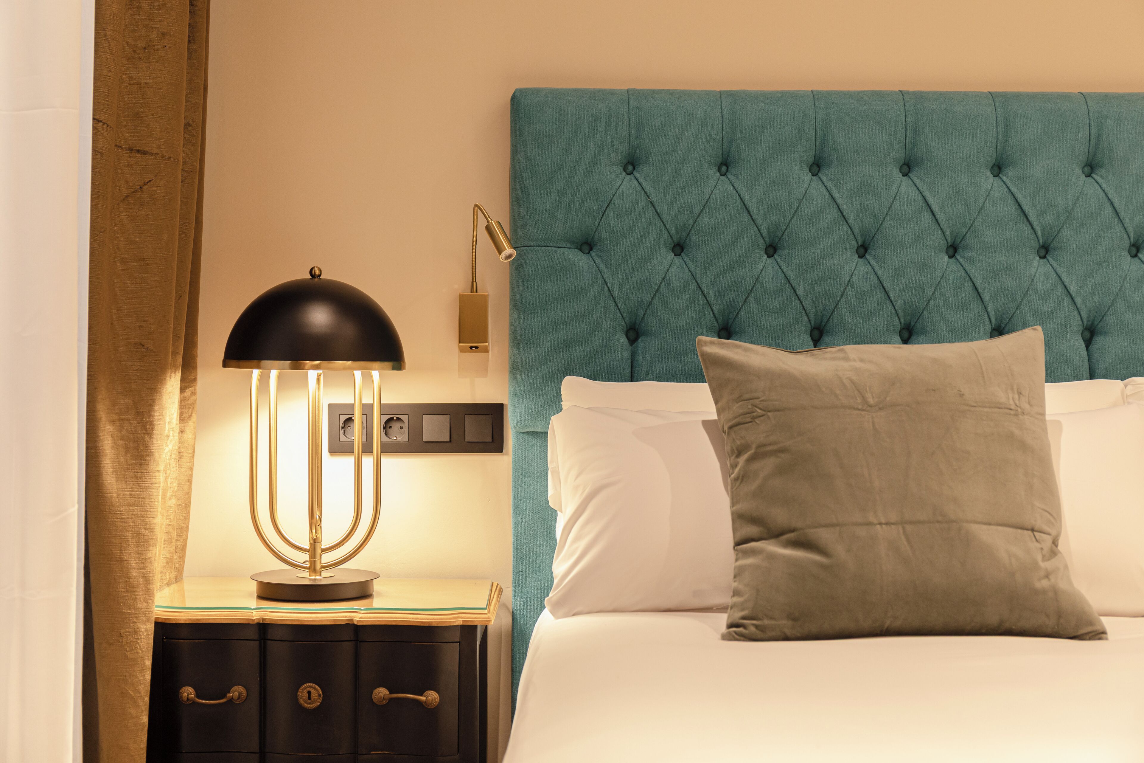 A neatly made bed with a tufted headboard, a bedside lamp, and a nightstand with drawers.