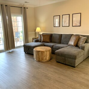 A living room with a sectional sofa, a round wooden coffee table, and a lamp on a side table.