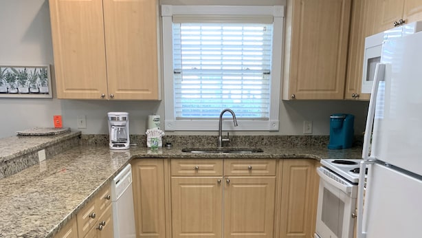 Una cocina con armarios de madera, horno empotrado, refrigerador y una ventana con persianas.