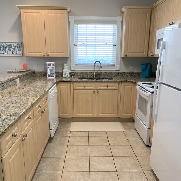 A kitchen with wooden cabinets, a built-in oven, a refrigerator, and a window with blinds.