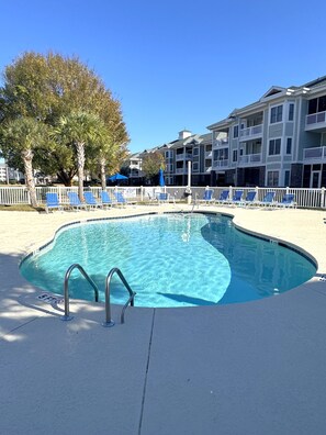 A swimming pool with a white deck, surrounded by lounge chairs and a white fence.