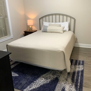 A neatly made bed with a headboard, a bedside lamp, and a patterned rug on a wooden floor.