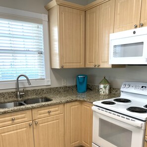 Una cocina con armarios de madera, un lavamanos de acero inoxidable, una estufa blanca y una ventana con persianas.