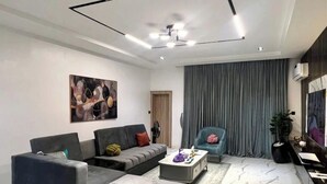 A modern living room with a sectional sofa, a chaise lounge, a coffee table, and a large painting on the wall. - Exclusive Sweet Green Rendezvous Hotel (Abuja)
