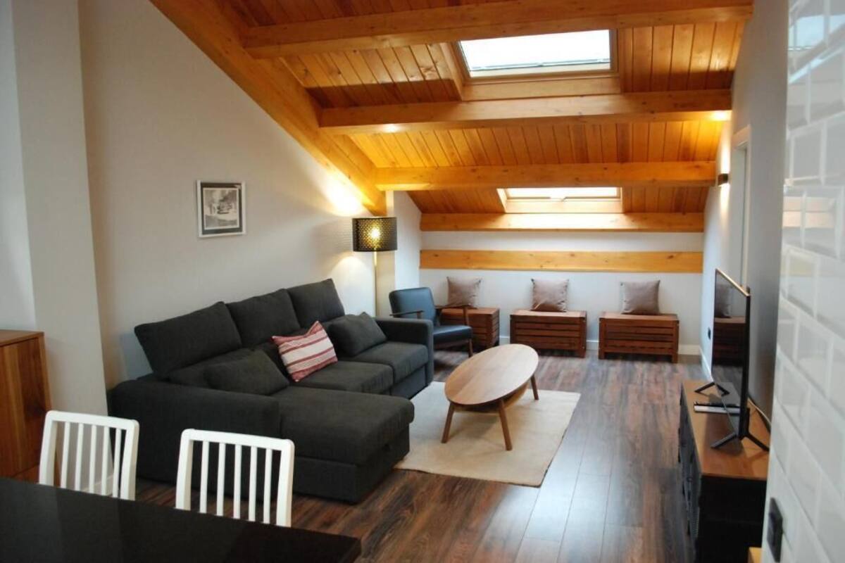 Una sala de estar acogedora con un sofá oscuro, una mesa de centro redonda y suelo de madera.