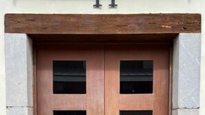 A wooden double door with six rectangular windows, a number '11' above it, and stone walls on either side. - Apartamentos Altar Suites Conde Luna (León)
