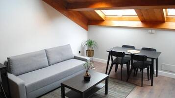 Una sala de estar acogedora con un sofá gris, una mesita con una planta y un comedor con una mesa y sillas.