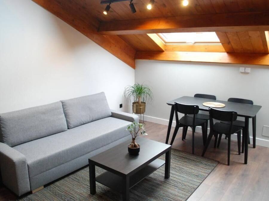 Una sala de estar acogedora con un sofá gris, una mesita con una planta y un comedor con una mesa y sillas.