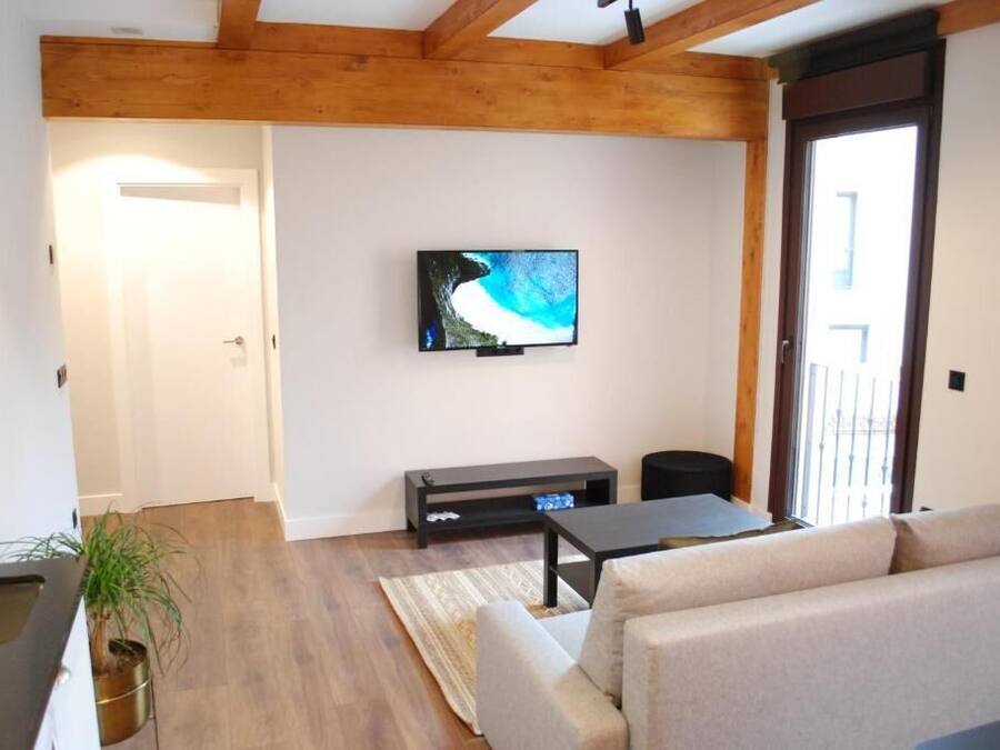 Ein Wohnzimmer mit an der Wand montiertem Fernseher, einer Couch, einem Couchtisch und Holzboden.