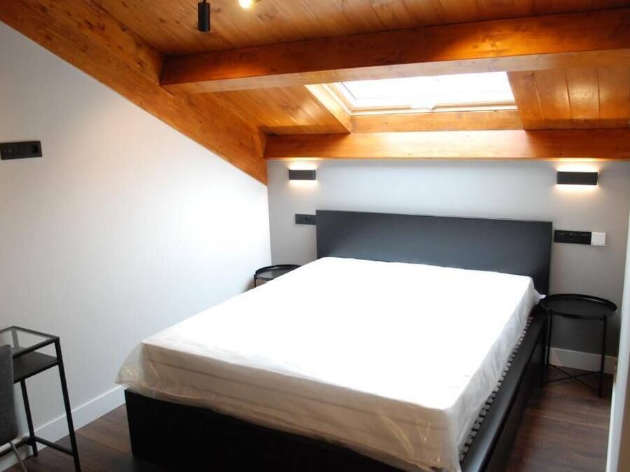 Un dormitorio con cama, tragaluz y una pequeña mesa.