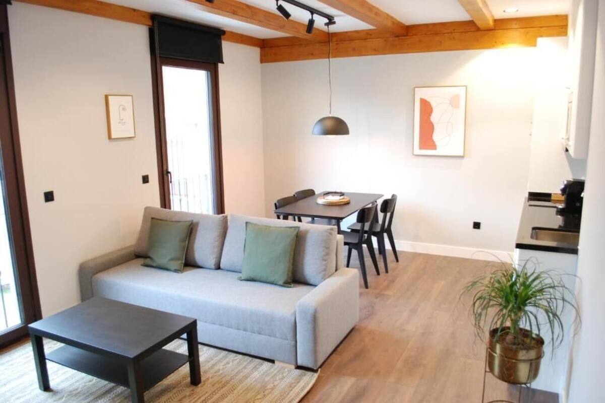 Un salon moderne comprenant un canapé, une table basse, une table à manger avec des chaises, un luminaire suspendu et un coin cuisine.