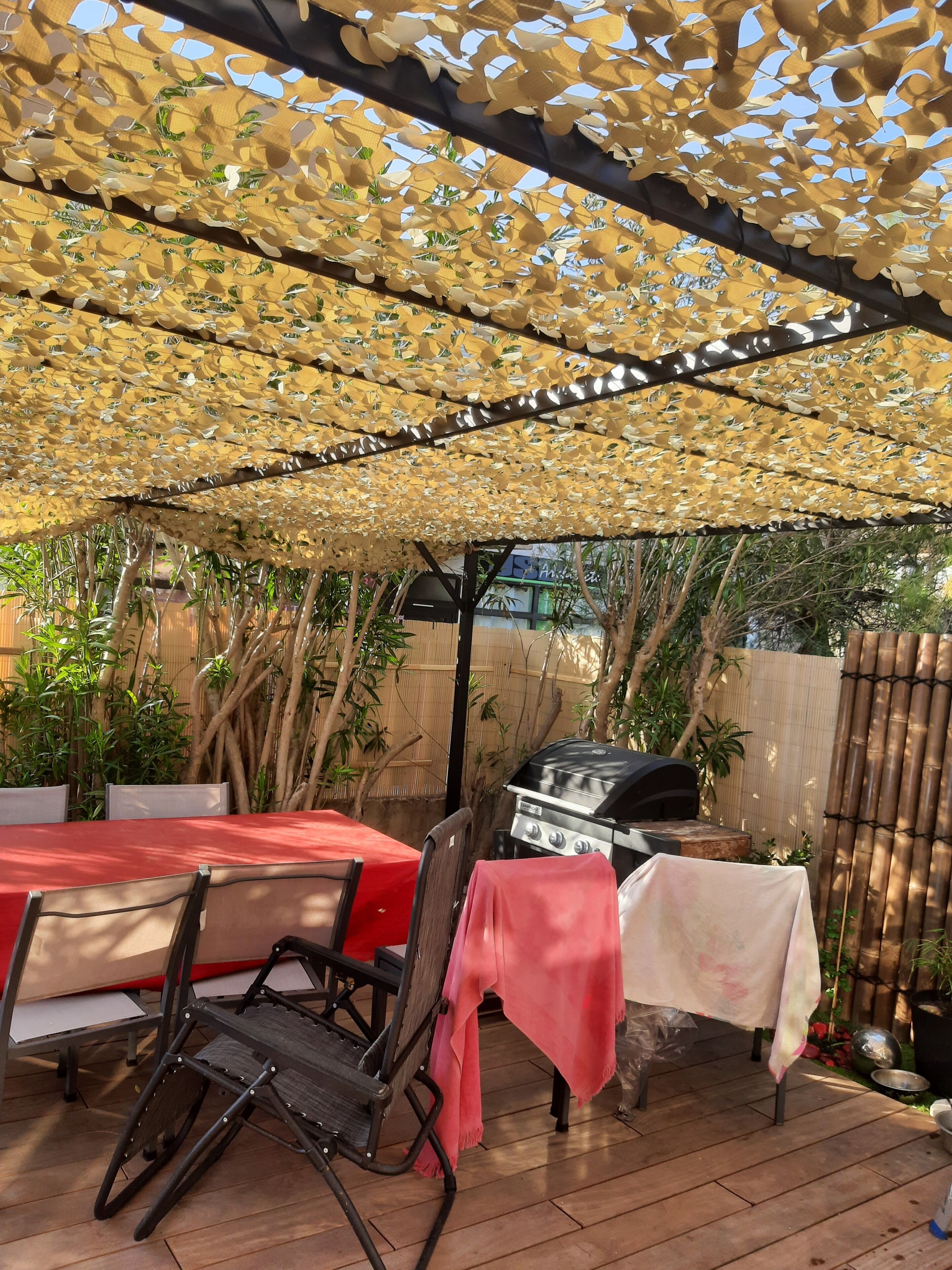 An outdoor patio with a grill, tables, and chairs under a shaded canopy.