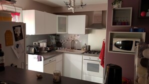 A kitchen with white cabinets, a sink, a stove, and a microwave. There are various kitchen items on the counter, including a toaster, a kettle, and a bottle. - Furnished 3-star house 300 metres from the sea, 84 m², 3 bedrooms (Hyères)