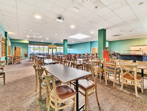 Una cafetería amplia con varias mesas y sillas, una máquina expendedora y una barra con un menú.