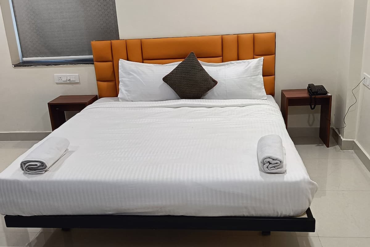 A hotel room with a bed, a nightstand, a phone, and a window.