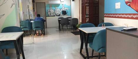 Un restaurante con sillas y mesas color turquesa, una persona al fondo y un mural en la pared.